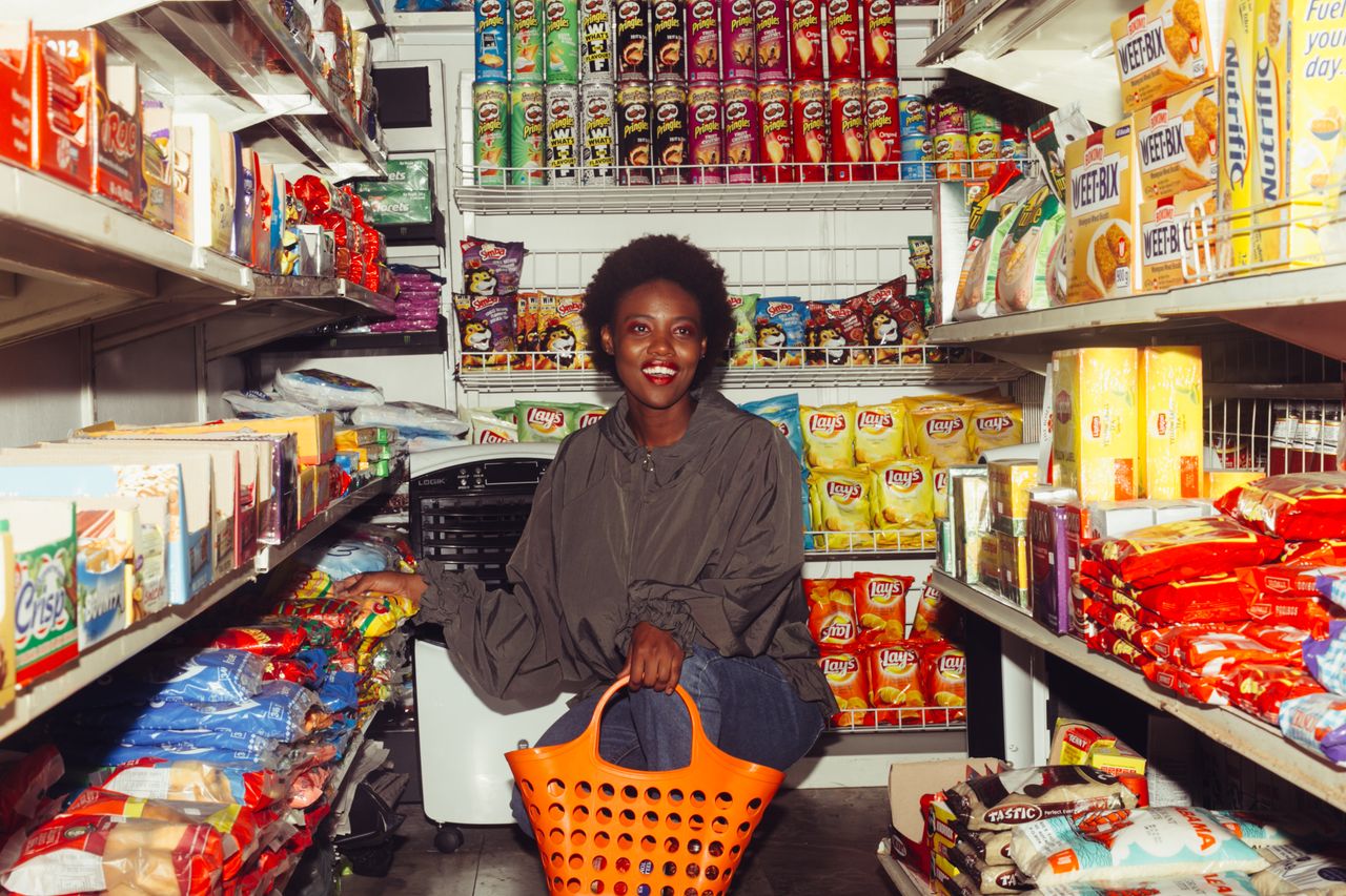 team-02 Full length of cheerful ethnic woman in casual clothes with shopping bag squatting among store shelves choosing food for buying